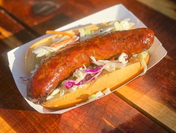 Grilled sausage hot dog with coleslaw in a bun on a wooden table.