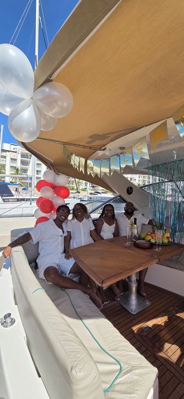 Four people celebrating a birthday on a yacht decorated with balloons and a banner.
