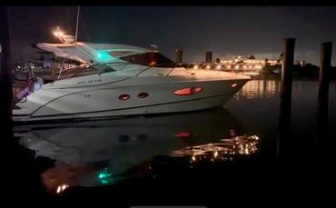 A white yacht docked at night with lights reflecting on calm water.