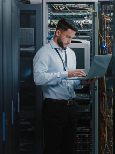 IT professional working on a laptop inside a data center server room.