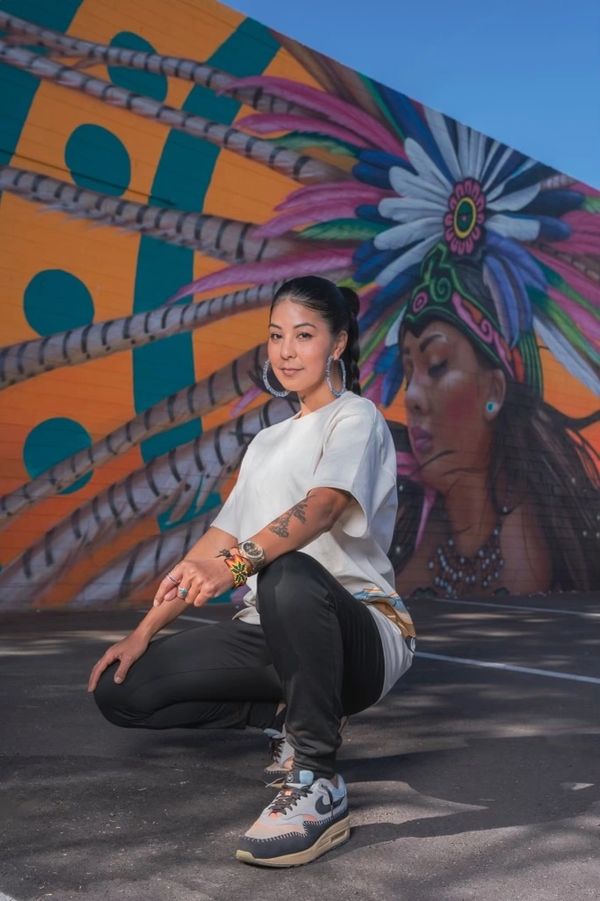Woman squatting in front of colorful mural with feathers.