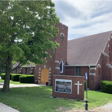 Red brick church building with a large tree in the foreground.