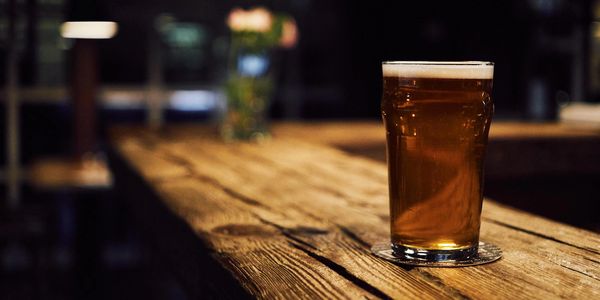 A pint of beer on a rustic wooden table in a dimly lit bar.