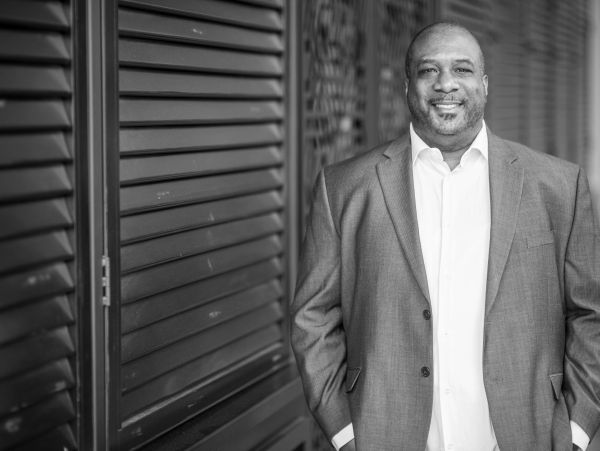 Confident man in a suit smiling while standing against a shuttered wall.