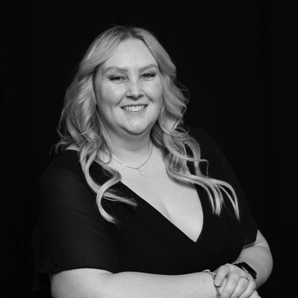 Smiling woman with blonde hair in a black dress against a black background.
