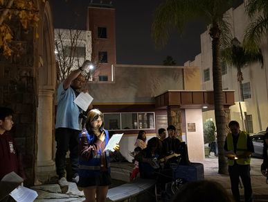 Young girl reading from a piece of paper to a crowd whilst being illuminated by a mans flashlight
