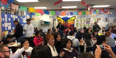 Students and teachers gathering in a classroom sitting down at different tables having fun