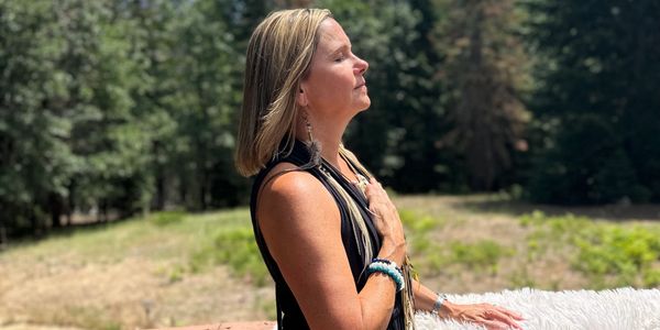 Woman meditates peacefully outdoors with eyes closed, hand on chest.