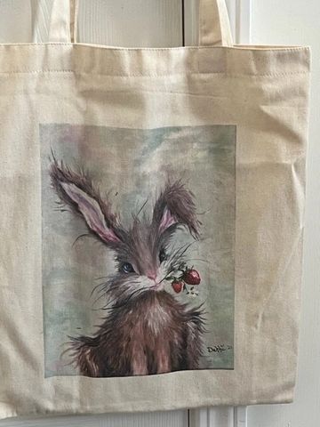 Photo of a canvas tote bag featuring a WhimzyWorks original painting of a whimsical bunny holding st