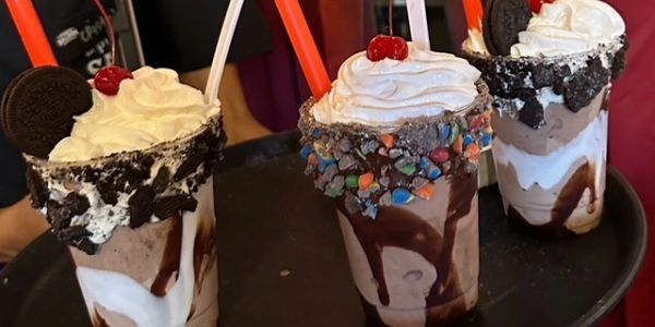 Three chocolate milkshakes topped with whipped cream, cherries, and cookies.