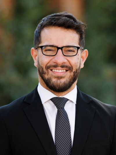 Smiling man in glasses and suit outdoors.