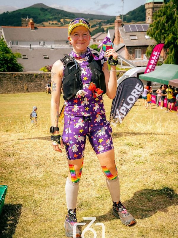 Runner in colorful outfit holding a medal and smiling.