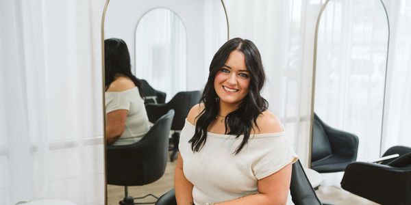Smiling woman with dark hair sitting in a modern salon chair.