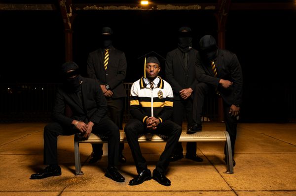 Man in a cap with four masked men in black suits.