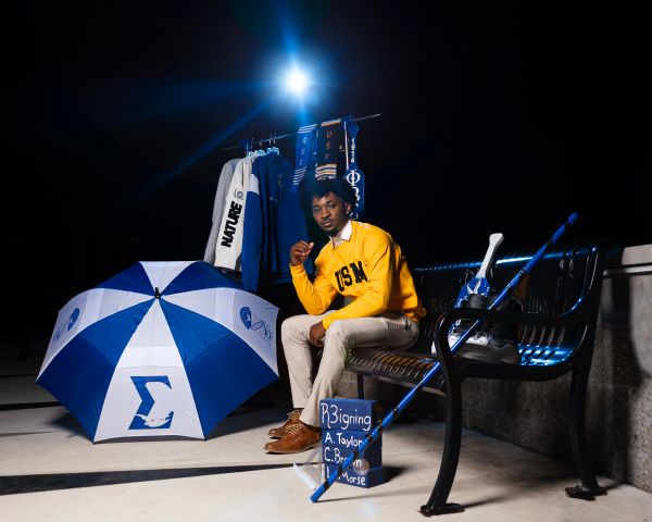 Man sitting on bench next to umbrella and sign.