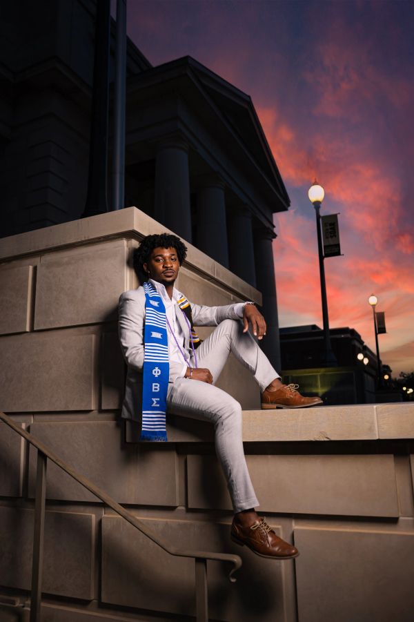 A man in a gray suit sits on steps during sunset.