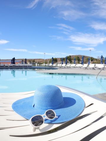 Hat and glasses resting by the commercial swimming pool with blue skies