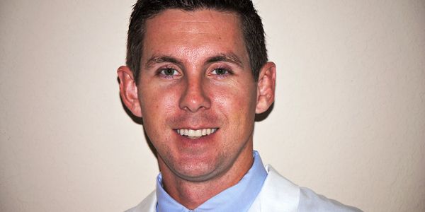 Man in a white coat smiling at the camera.