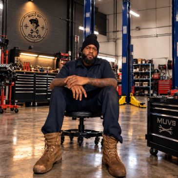 Man in a mechanic workshop sitting on a stool.