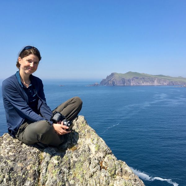 Photo shows Isobel sat on a rock with the see and sky behind her.