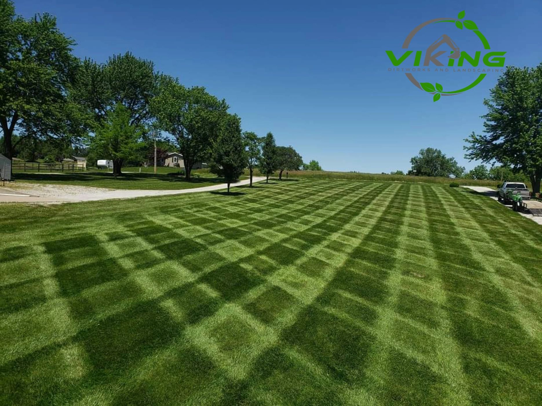 A large lawn with a checkered mowing pattern under a clear blue sky.