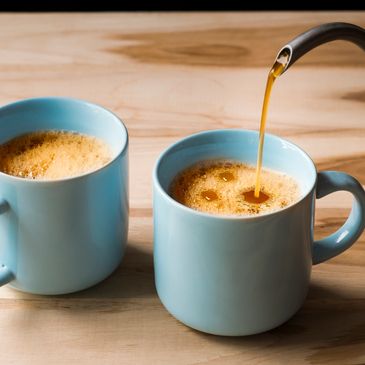 Hot coffee being poured for two cups on a table