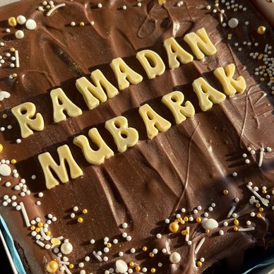 Chocolate cake decorated with white letters spelling 'Ramadan Mubarak'.
