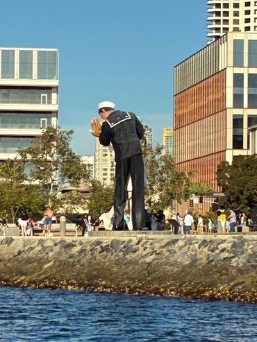 Statue of a sailor kissing a nurse by the waterfront with city buildings behind.