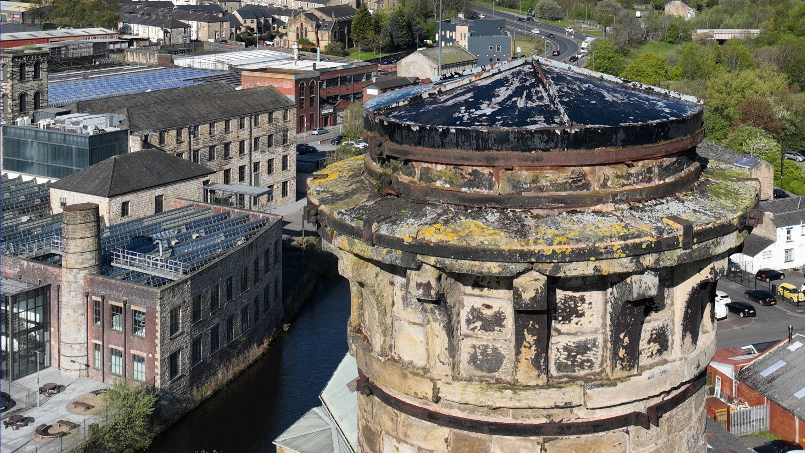 Aerial view of an old stone chimney and surrounding industrial buildings near a water canal.