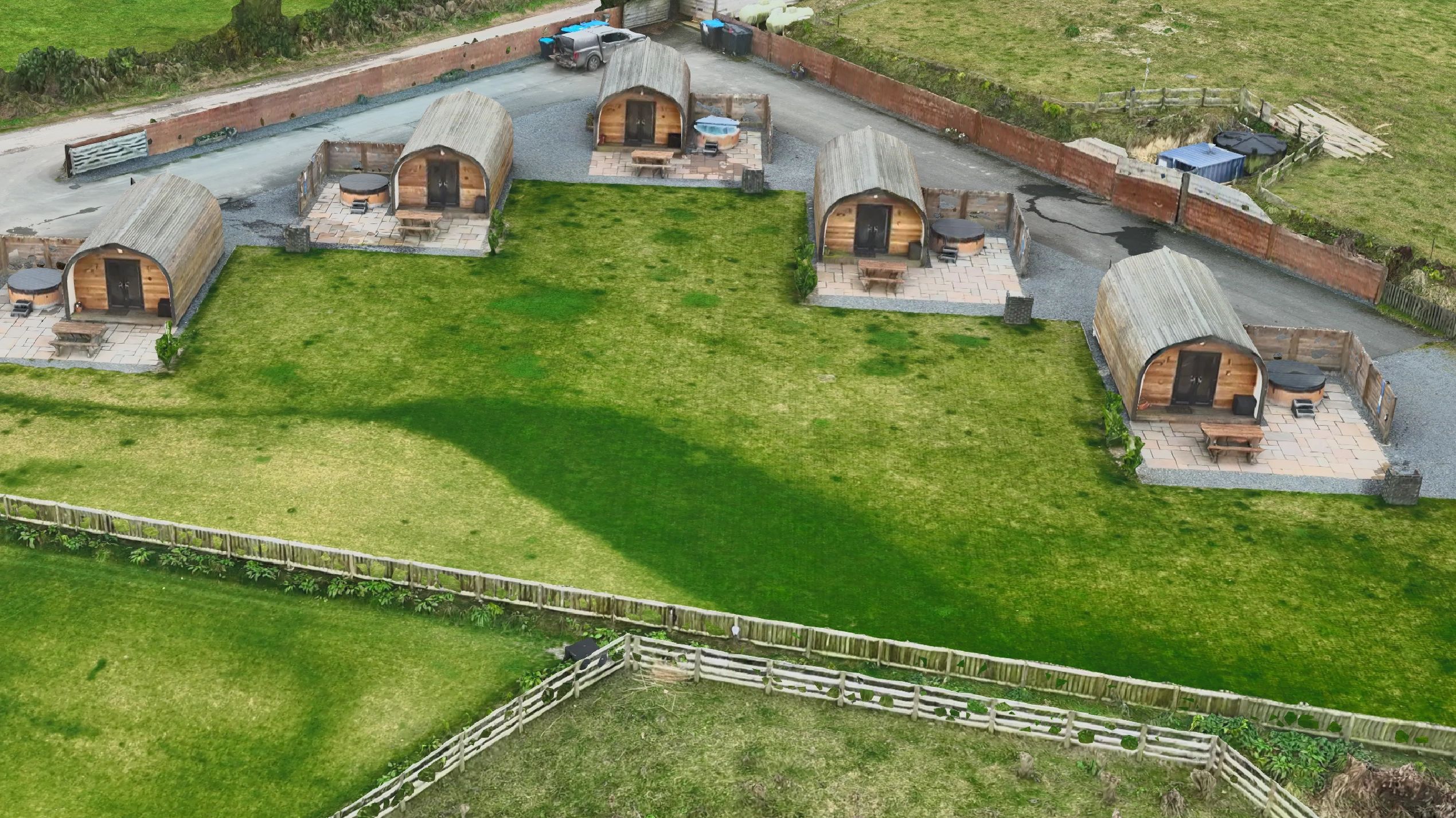 Aerial view of five wooden pod cabins with outdoor seating and hot tubs.