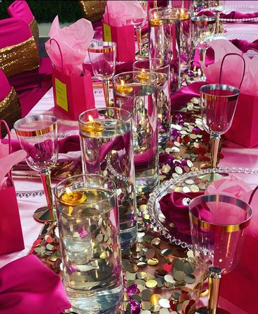 Elegant pink and gold-themed table setting with candles and gift bags.