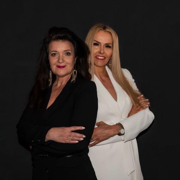 Two confident women posing together against a black background.