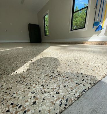 Close-up of a polished, speckled garage floor with sunlight streaming through windows.