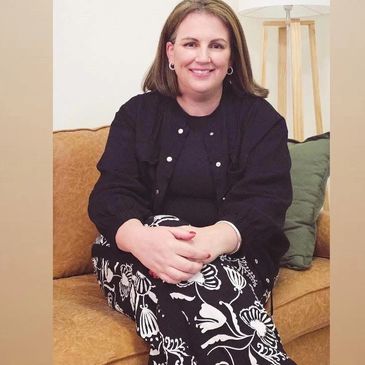 A photo of Cate, Social Worker and Director at Wellbeing Support Space. Sitting on a brown couch. 