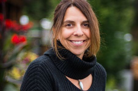 Woman wearing black sweater, smiling with flowers ie background