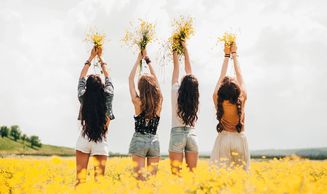 Four Young women standing in a field of yellow flowers holding bunches of flowers above their heads