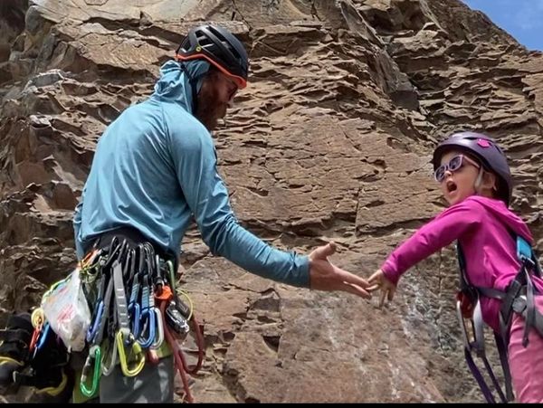 An adult and child rock climber reaching out to each other on a rocky cliff.