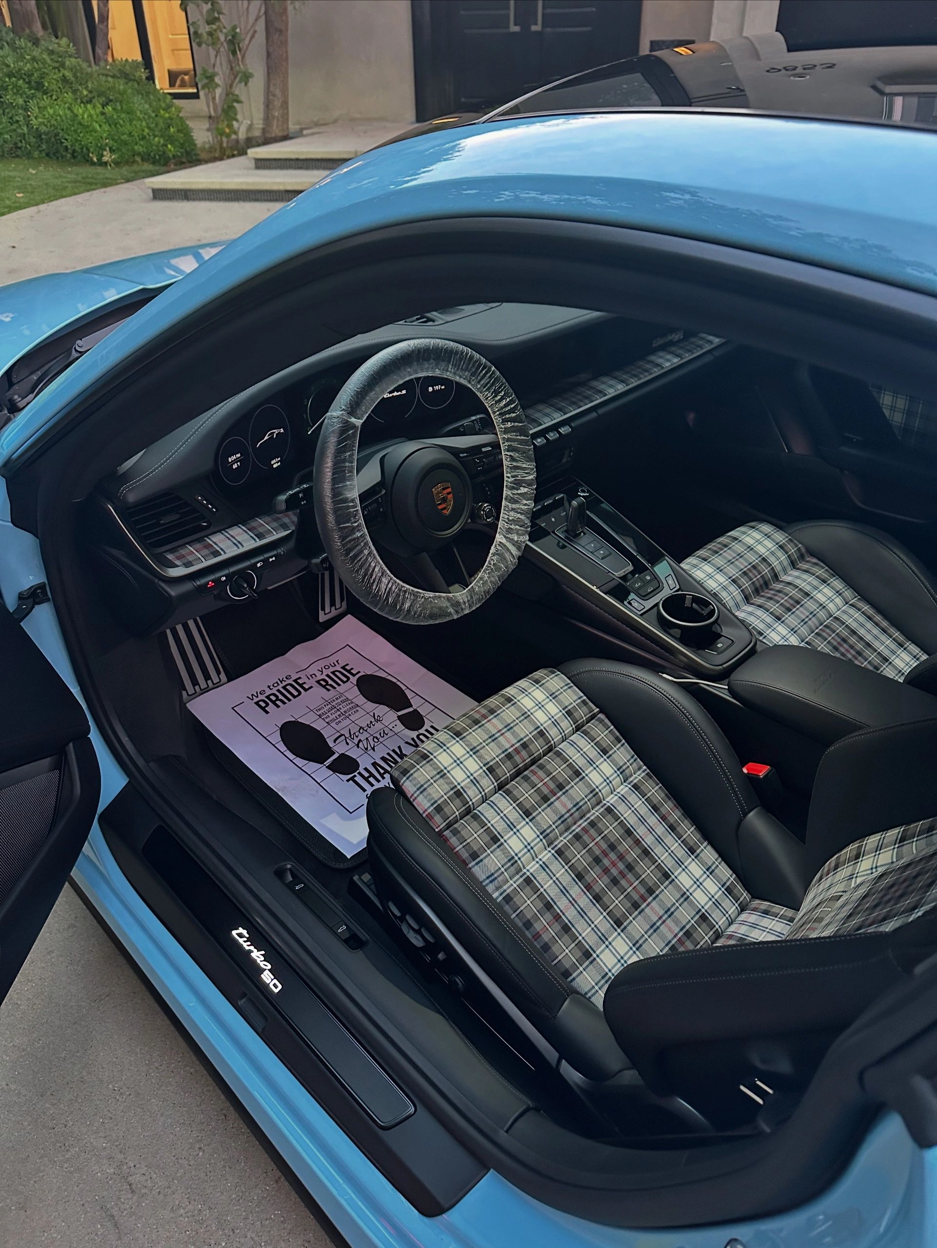 Interior of a Porsche Turbo S with plaid seats and a protective steering wheel cover.
