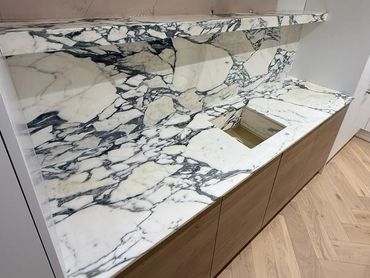 Marble countertop with integrated backsplash and wooden cabinets.