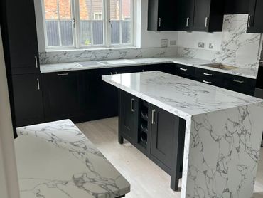 Modern kitchen with black cabinets and white marble countertops.