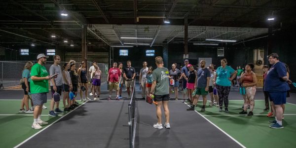 Group of people gathered on an indoor pickleball court.