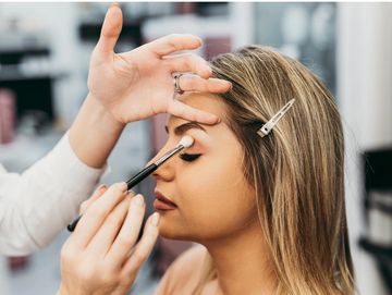 A woman getting eye makeup applied with a brush.