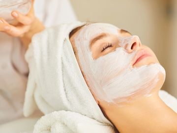 Woman relaxing with a white facial mask and towel on her head.