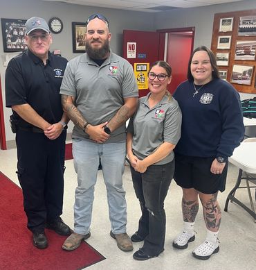 Four people standing and smiling inside a fire department meeting room.