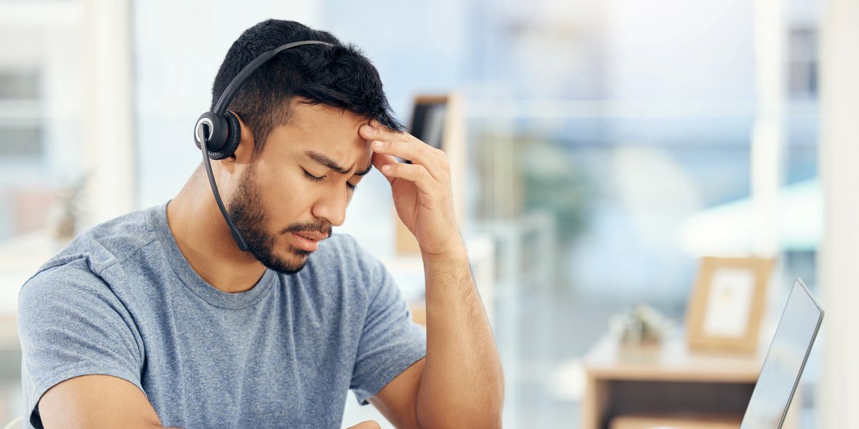 Man with headset looking stressed and holding his forehead.