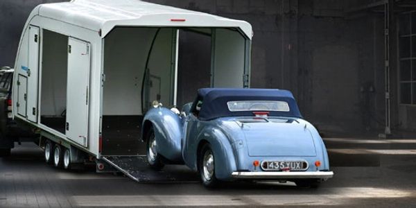 Classic car being loaded into the rear of the covered car trailer with side door also open.