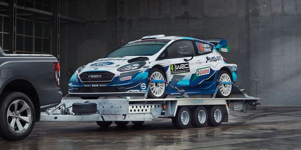 Open car trailer being used for motorsport. Rally car strapped down onto the trailer.