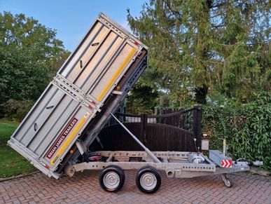 Electric Tipper trailer in the tipped position while unhitched to a vehicle. In a driveway setting.