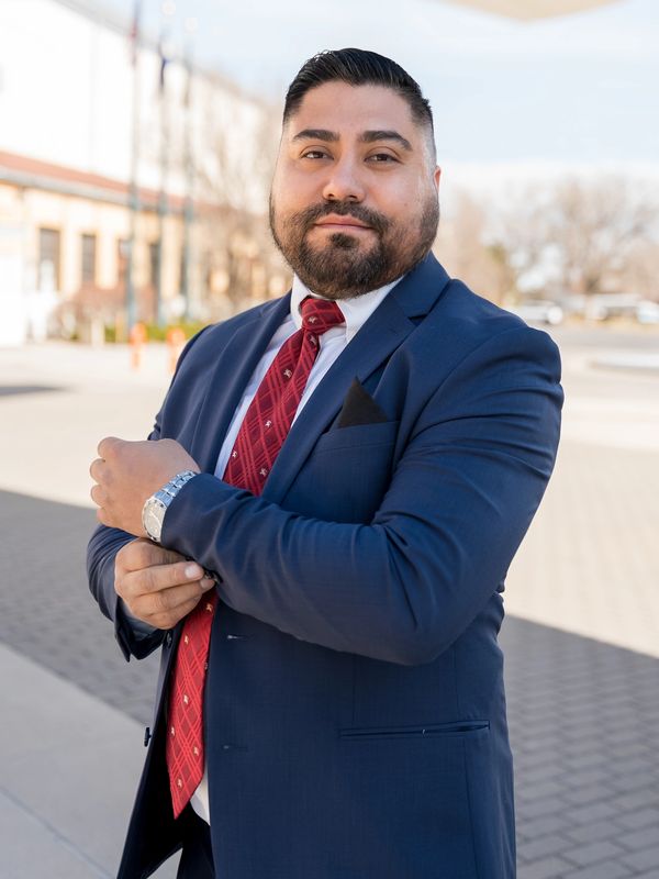 Man in a navy suit adjusting his watch outdoors.