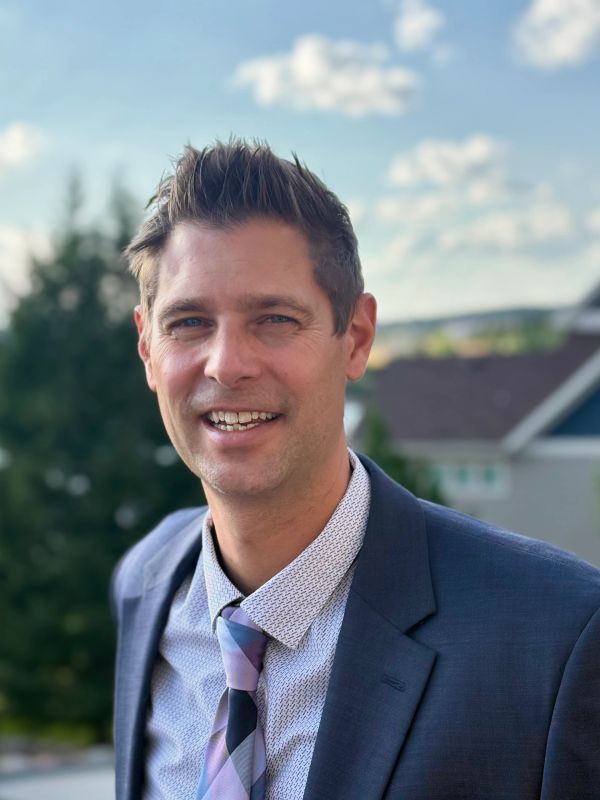 Man in suit smiling outdoors with blue sky.